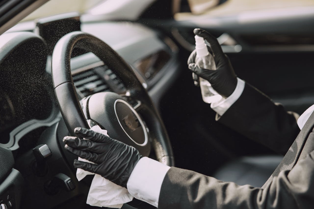 about-us A person in gloves disinfecting a car steering wheel for hygiene and safety.