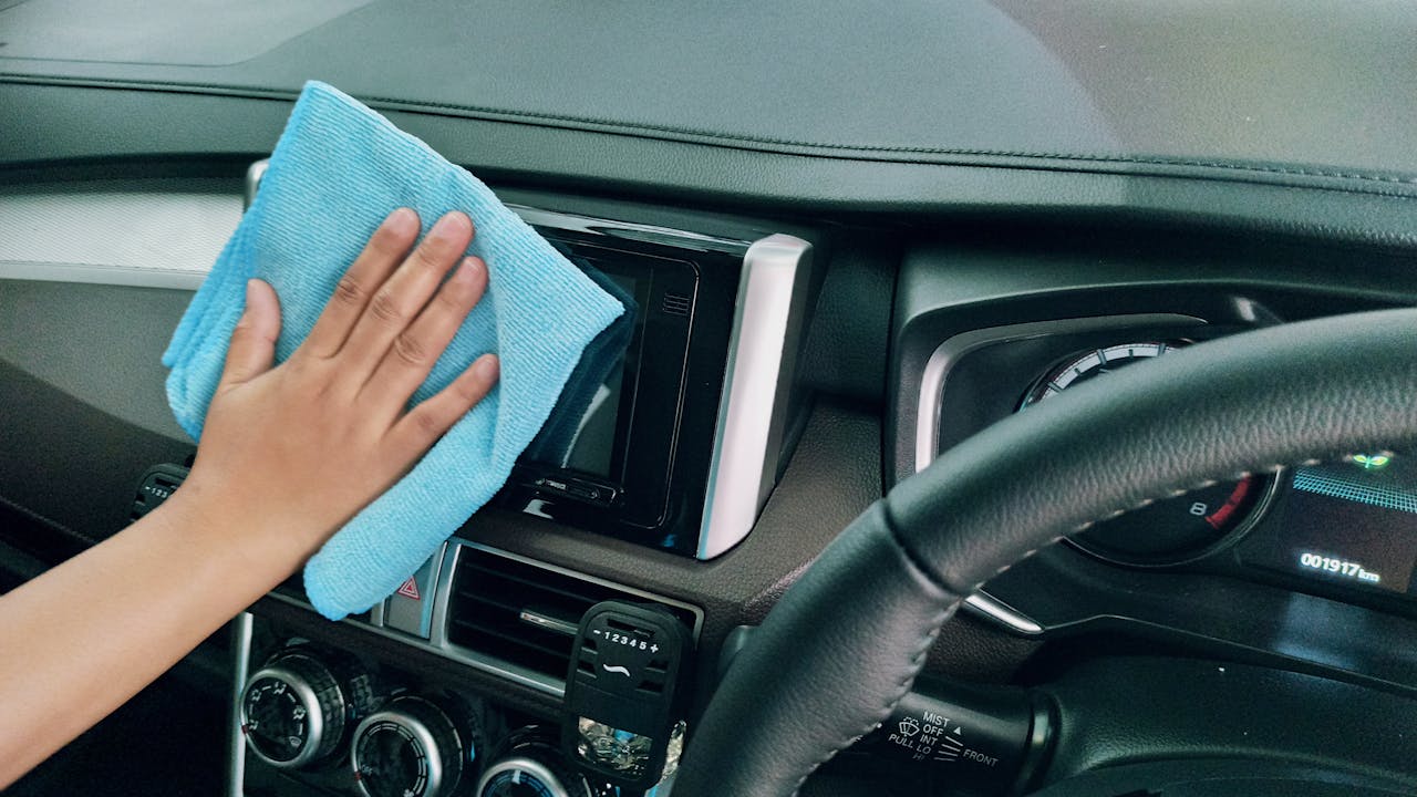 heros-img Close-up of a hand cleaning a car dashboard with a blue microfiber cloth.